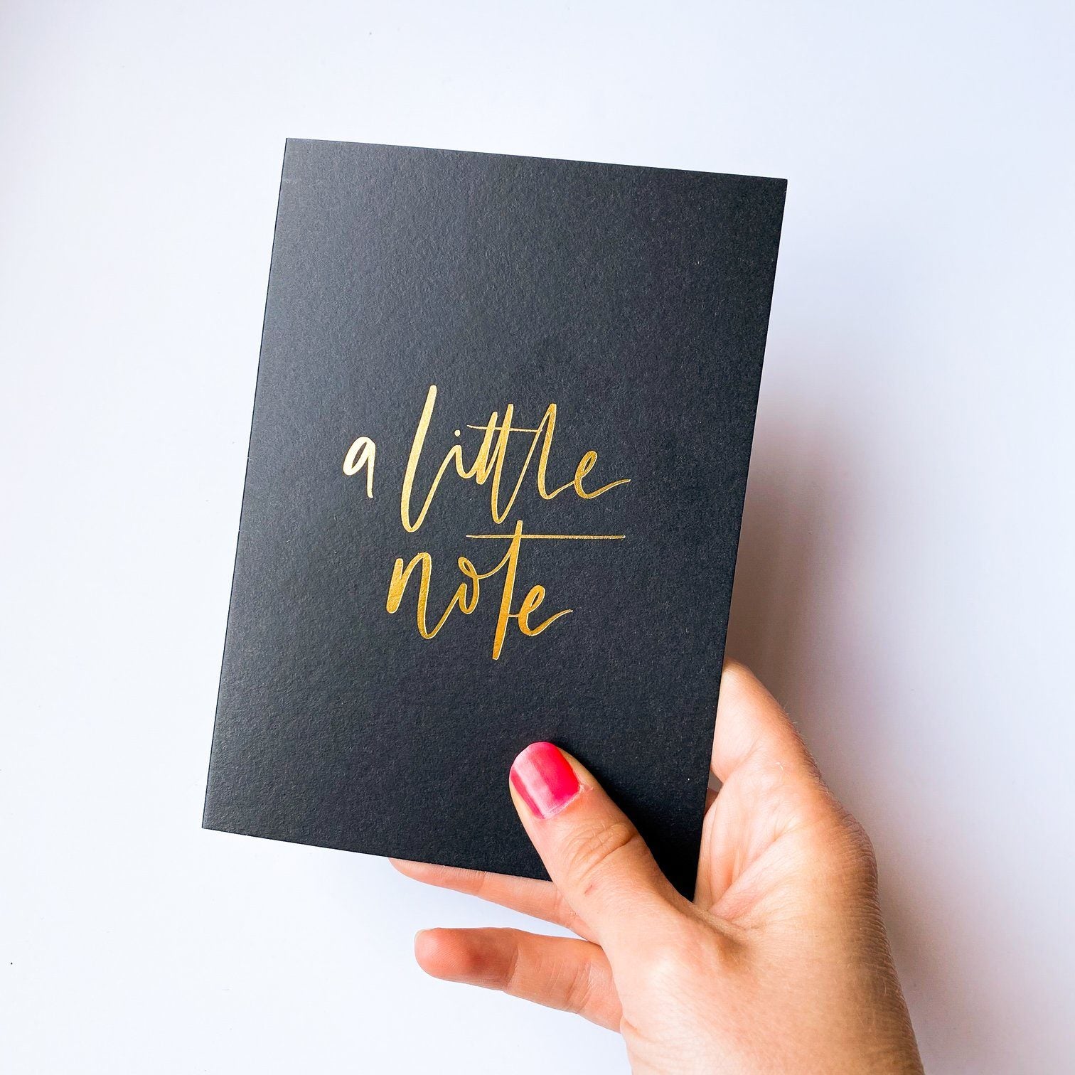 Gift Card - Photo of a hand holding a black occasion card that states "A little Note!" in gold foil